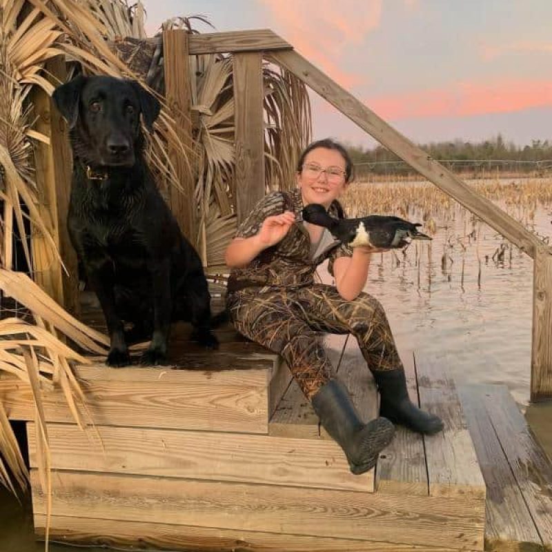dog and young adult sitting on steps at lake holding a duck