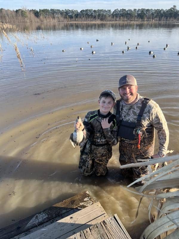 man and son standing in lake holding a duck